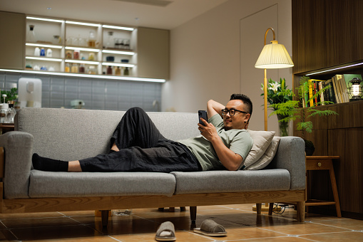 Asian middle-aged man lying on the sofa looking at his phone