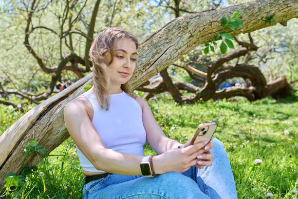 istock Young female sitting on grass in park, relaxing with smartphone 1553390020