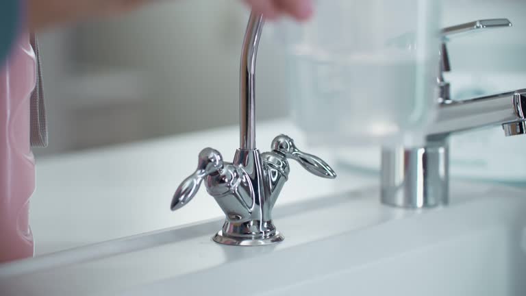 Close-up of a filter faucet in the kitchen. A woman’s hands open the faucet and draw filtered water into a container.4K