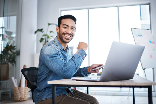 istock Business man, laptop and smile in startup office, web design or planning with pride for entrepreneurship. Asian businessman, pc or happy content creator for coding, programming or website development 1553414526