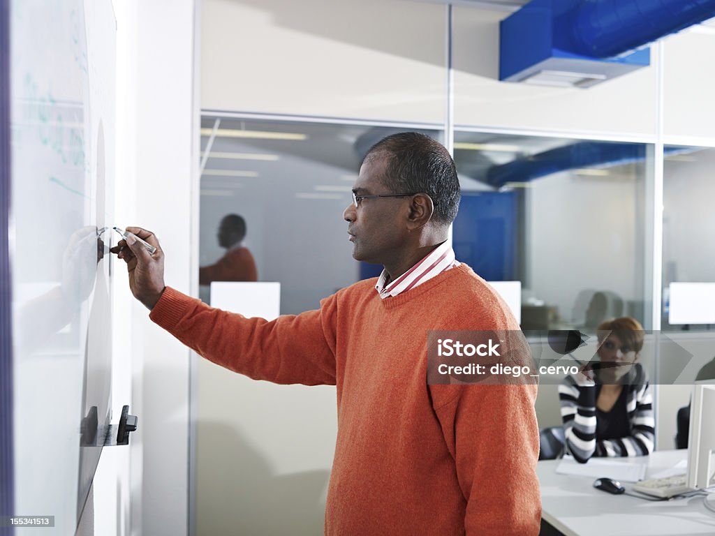 A teacher writing on the board inside the computer lab Computer class with indian male teacher writing on board and students in background. Horizontal shape, side view, waist up 20-29 Years Stock Photo