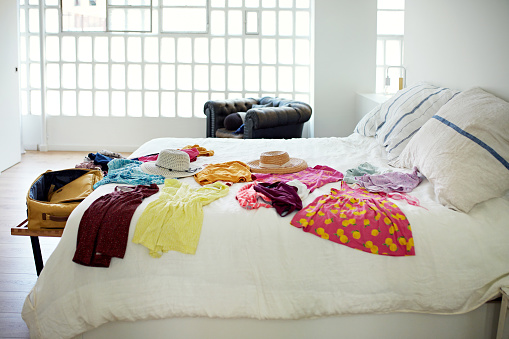 Clothing and hats laid out on bed in unoccupied home interior, ready for leisure travel.