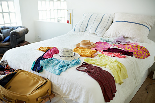 View of warm weather tops and dresses, swimwear and hats, all laid out on bed in unoccupied domestic room and ready for leisure travel.
