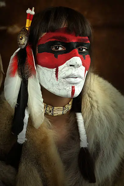 Native american woman portrait with painted face. Young beautiful woman in native american costume with wolf fur and war mask on her face