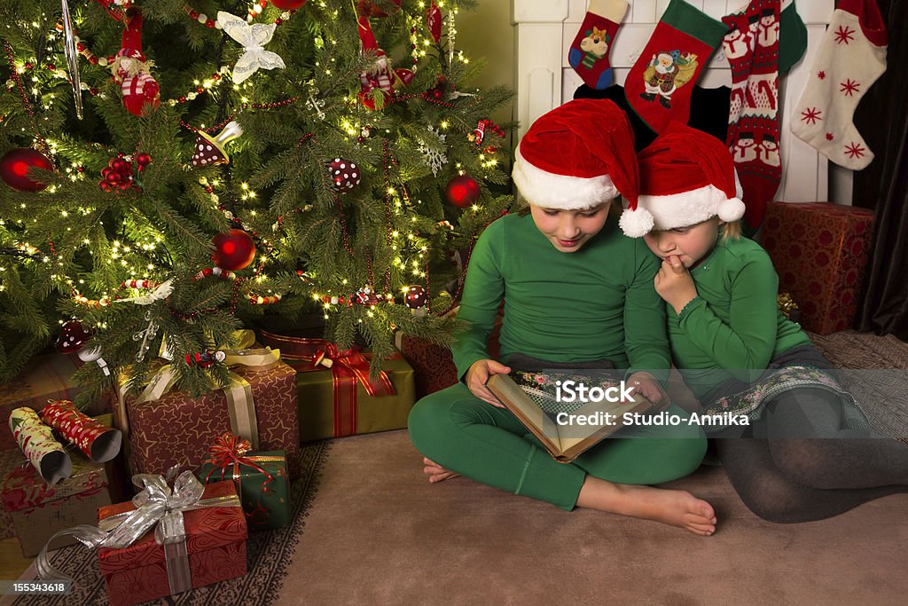 Reading christmas stories Two little girls reading in a book near the christmas tree Book Stock Photo