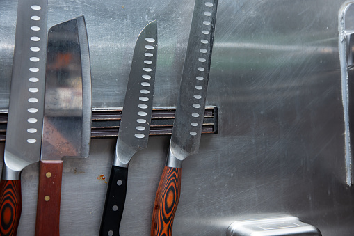 A view of several professional chef knives on a magnet wall mount in a restaurant kitchen.