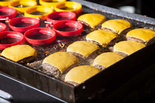 A view of an outdoor griddle cooking up cheeseburgers.