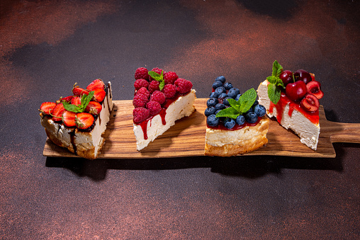 Summer cafe baking menu background, sweet cheesecake portion slices with various toppings, jam and berry fruits - strawberry, blueberry, raspberry, cherry