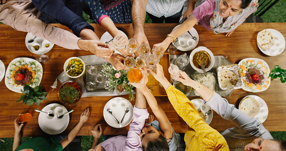 Big Indian Family Lunch Table: Top Down Elevated View at a Family and Friends Celebrating Outside at Home.Group of Children, Adults and Seniors Raising their Glasses to Clink them and Make a Toast