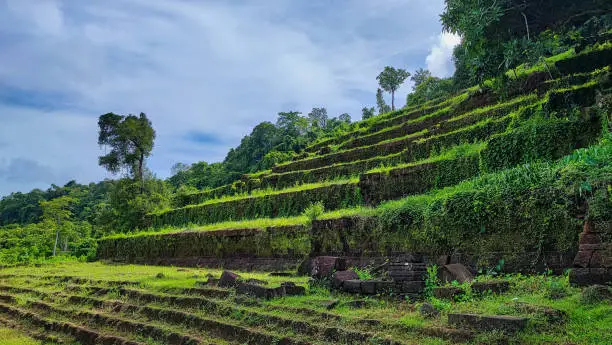 Photo of The beautiful view landscape of the green grass cover ancient spiritual brick stairs in Wat Phou/vat Phou Hindu temple complex is the UNESCO world heritage site in Champasak, Southern Laos.