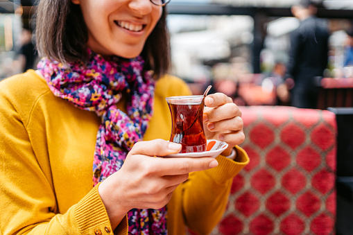 Young cheerful woman sitting and drinking Turkish tea in a café in Istanbul.