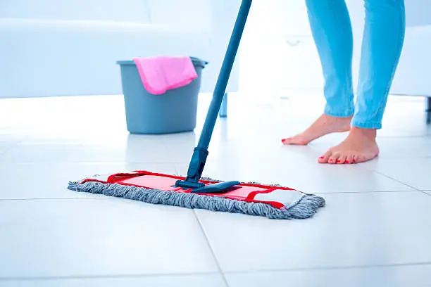 Woman cleaning tiled floor using mop.