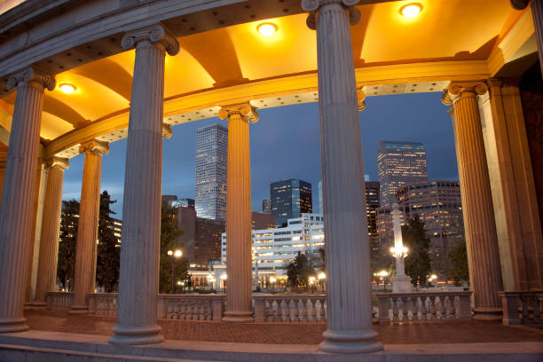 Nighttime Downtown Denver Skyline Civic Center Park Colorado At dusk, the downtown Denver skyline lights up looking through columns of the Greek temple in the Civic Center Park. A Denver landmark, original construction of Civic Center Park was 1912 - 1920 and since, has been placed on the National Register of Historic Places. civic center park stock pictures, royalty-free photos & images