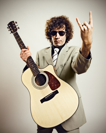 Man with long hair wearing white denim jacket, blue pants, black shirt and black Matsuda sunglasses, playing white electric guitar