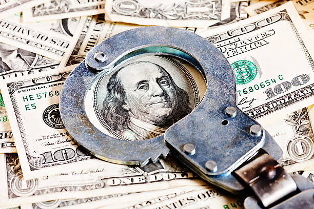 Handcuffs circle Benjamin Franklin in stack of dollars Looks like crime doesn't pay! A pair of handcuffs rests, with the bracelet circling the face of Bejamin Franklin, on a US $100 bill topping a stack of money. white collar crime handcuffs stock pictures, royalty-free photos & images