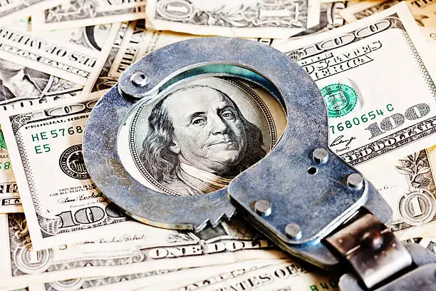 Photo of Handcuffs circle Benjamin Franklin in stack of dollars