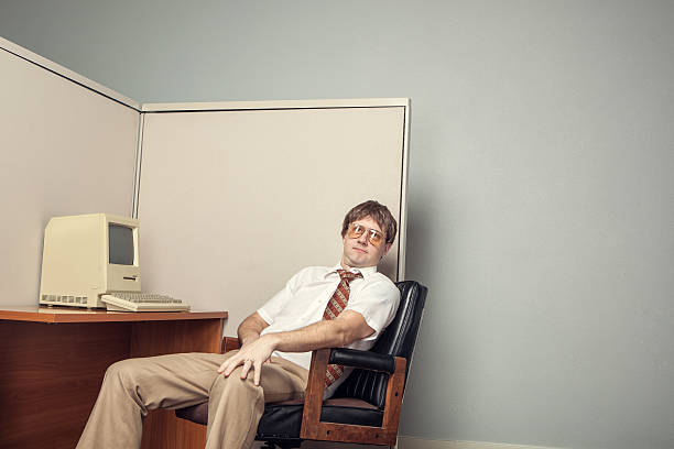 Eighties Computer Tech Nerd A lazy I.T. computer technician leans back in his chair in his office cubicle sitting in front of his desk with a vintage 1980s computer.  Horizontal with copy space. office cubicle photos stock pictures, royalty-free photos & images