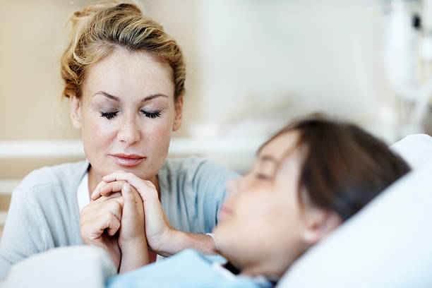 dizer o silencioso orações de esperança - mother and daughter holding hands on bed - fotografias e filmes do acervo