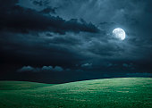 Hilly meadow at night with full moon, clouds and grass