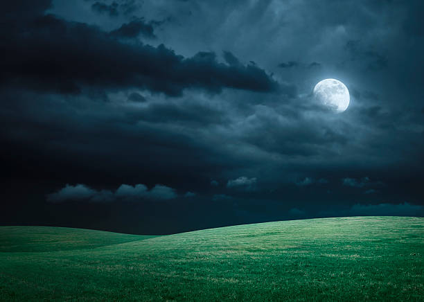 Hilly meadow at night with full moon, clouds and grass stock photo
