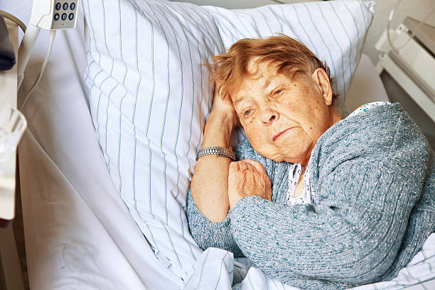senior woman in hospital senior woman, 87 years old, in hospital, lying in bed, wearing a woolen jacket, with worried expression sick woman hospital bed stock pictures, royalty-free photos & images