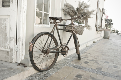 An old bicycle in Cape Town South Africa rests against a wall on a quiet street.  Street is brick and it is leaning against a white and grey wall.  Subdued colours.  Leica Camera Image.