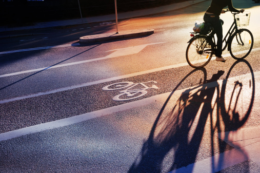 Bike lane in evening. Sign for bicycle painted on the asphalt. Car and traffic in background. Dividing line. Shadow from sunset sun.