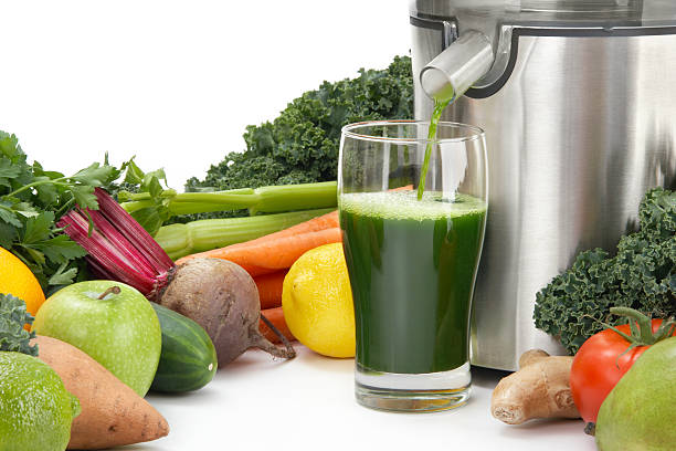 Juicer pouring juice into glass surrounded by vegetables stock photo