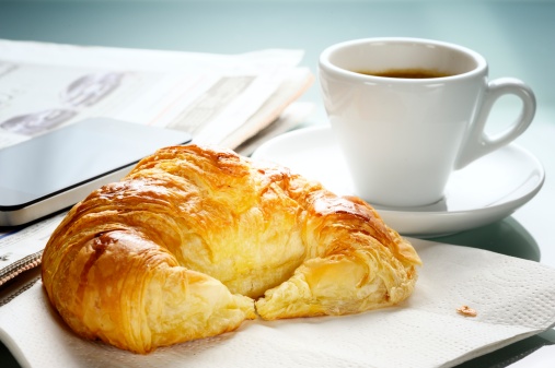 French breakfast consisting of espresso coffee and a freshly baked croissant. Time to read the newspaper and consult the smartphone.