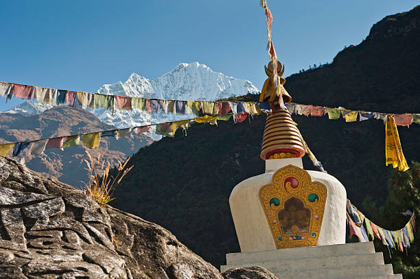 Traditional white-washed stupa shrine and colourful Buddhist prayer flags under the snow capped mountain peaks of Thamserku (6623m) and blue Himalayan skies deep in the Everest National Park, Nepal. ProPhoto RGB profile for maximum color fidelity and gamut.