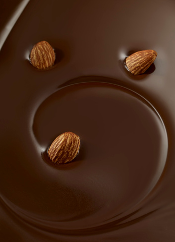 Full frame photo of almonds dipping in a liquid chocolate swirl