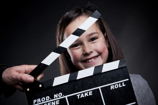 Happy child with movie clapper board, over black background.