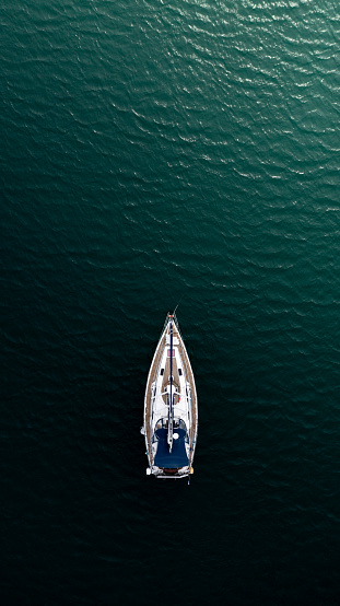 Aerial view directly above a luxury sailing yacht emerging from the darkness and sailing towards the light in a concept of hope