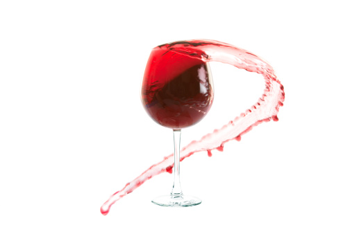Red wine in a glass splashes on the walls of the glass on a white background and a black reflecting table.