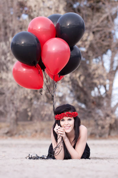 Beautiful young woman with long black hair sitting on sandy beach with red balloons.