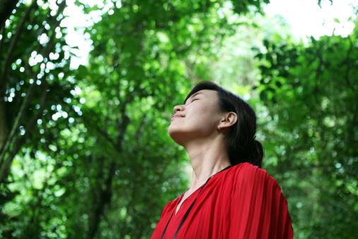 A beautiful woman is taking a deep breath and listening the sound of bird in the forest at morning