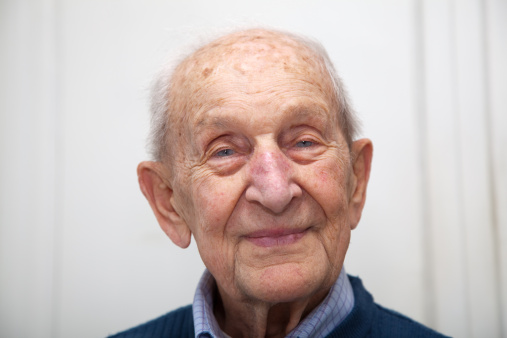 Senior male portrait 90 years old close up of his face with a diffuse whitish background shot in his kitchen from a slightly lower angle to emphasize his sparkling blue eyes.