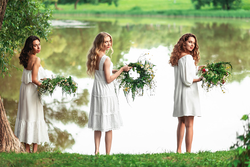 Three girls in white dresses with a wreath of flowers are celebrating Ivan's Day or Ivan Kupala's holiday.