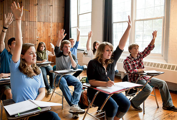 High school students raising their hands in a classroom A classroom of high school students raising their hands. hand raised classroom student high school student stock pictures, royalty-free photos & images