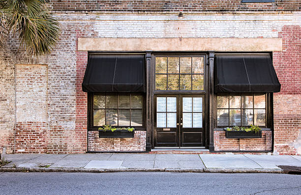 Colonial Storefront with awnings Colonial Storefront with black awnings with old brick wall, window boxes and cracked pavement. store stock pictures, royalty-free photos & images