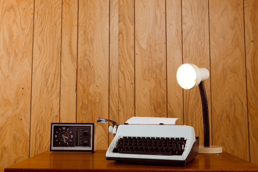 Horizontal image of a 1970s office desk. Complete with typewriter, lamp and clock/radio.