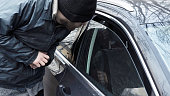 Homeless thief steals purse valuable items from car with unlocked doors open. Property insurance against unlawful theft or crime. Male burglar looks through crack in window. Auto without alarm system