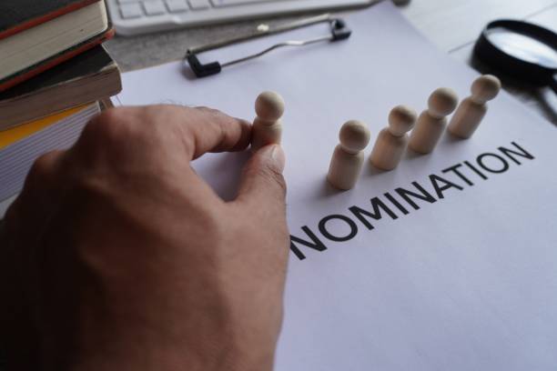 istock Hand pick wooden doll and text NOMINATION. 1553562527
