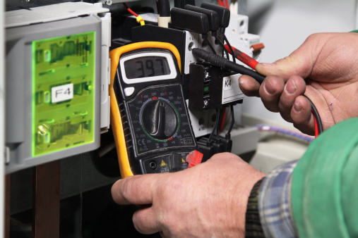 Electrician checking electric potential with a digital multimeter in an industrial voltage panel.