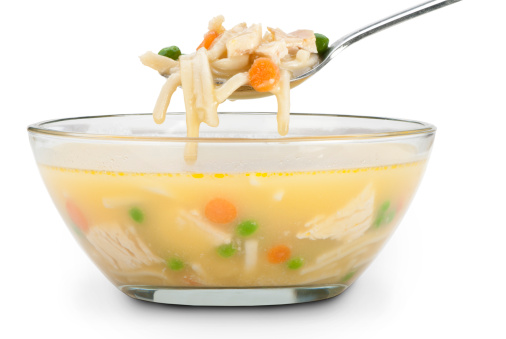A hearty clear glass bowl of chicken noodle soup with a spoonful showing all of the ingredients. Background is 255 white with a clipping path.