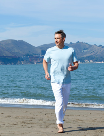 handsome mature man running on the sand, with ocean in background