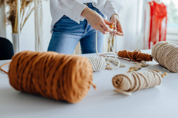 istock Creative hobby handmade macrame for home decoration. Close up of women's hands weaves macrame. Handmade macrame belt in work process. Female hobby. 1553571930
