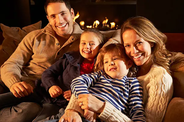 Portrait family relaxing at home by firelight smiling to camera