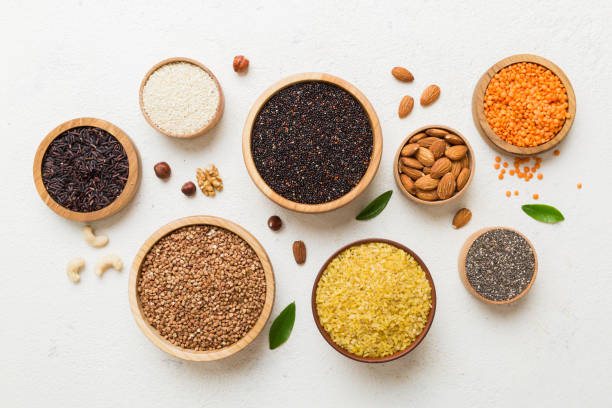 varios superalimentos en tazón pequeño sobre fondo de color. superalimentos como arroz, chía, quinoa, lentejas, nueces, semillas de sésamo, almendras. espacio de copia de vista superior - sesame seed spoon variation fotografías e imágenes de stock