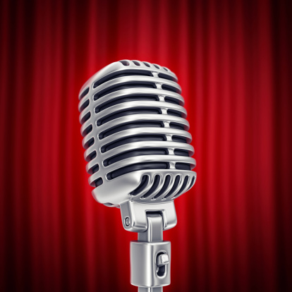 focus on the vintage silver microphone and blured red stage curtain in background.